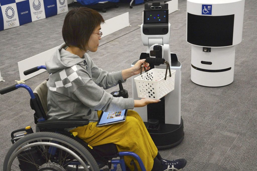A robot hands a basket containing drinks to a woman on March 15, 2019 during an event in Tokyo tied to the upcoming Olympics.