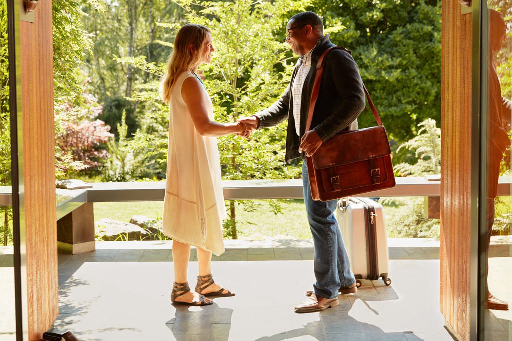 Airbnb is eliminating guest fees for many properties around the world so it can better compete with Booking Holdings. Pictured is an Airbnb host greeting a guest.