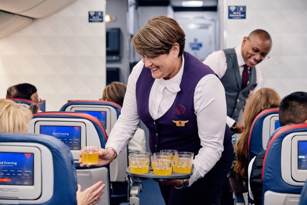 Shown here, a Delta flight attendant offers complimentary Bellini cocktails to passengers. In November 2019 Delta launches upgrades to the economy cabin experience for international long-haul flights.