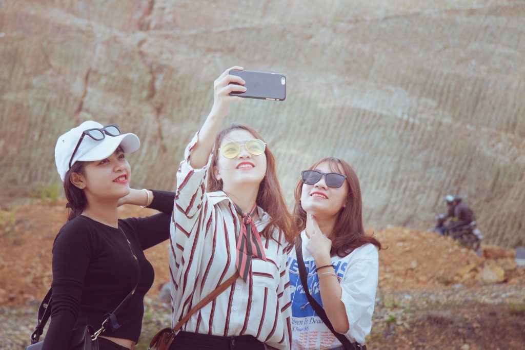 Millennial and Gen Z travelers from India and China are avid and optimistic travelers. In the photo, three young women take a selfie on a smartphone.