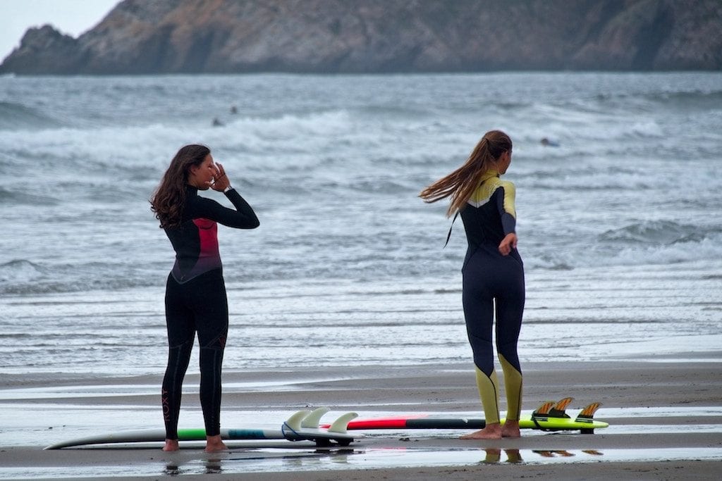 Two women are shown surfing. Women-only wellness travel has taken off in 2019.
