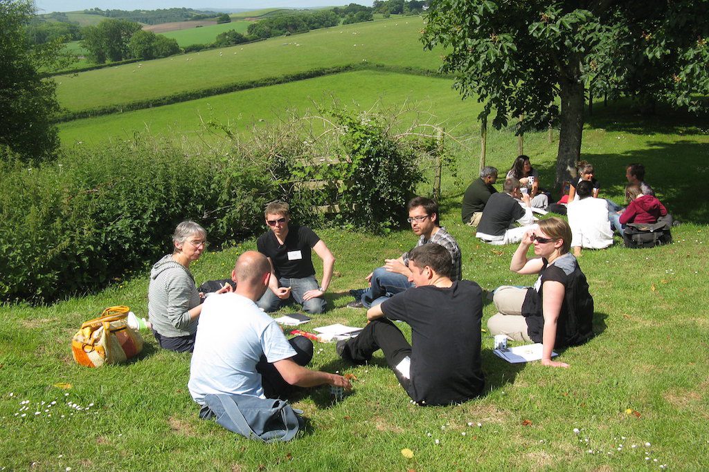 Event attendees sit in small groups outside at a venue in Devon, England. Meeting planners are beginning to choose less popular locations for events in response to overtourism.