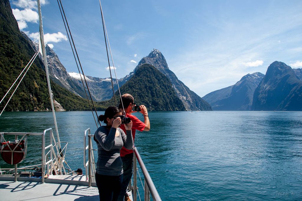 Tourists take photos of the Milford Sound, a fjord off the southwest coast of New Zealand's South Island. Corporate travel can be challenging, but tacking on leisure can help relieve the strain and improve personal lives of employees.