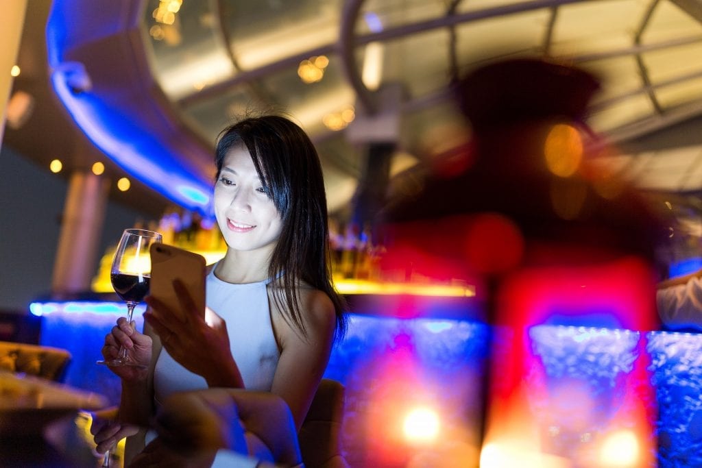 Woman looks at her mobile device while having a glass of wine at the Sky Bar. As luxury travel marketing expands in China, international brands are learning that both the messaging and the technology used to share messaging matters.