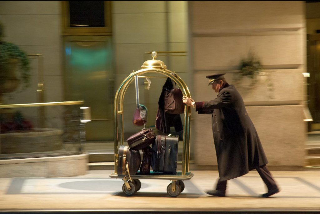 Pictured is a hotel concierge pushing a luggage cart. Skift Research forecasts a a year of slower but positive growth for hotels.
