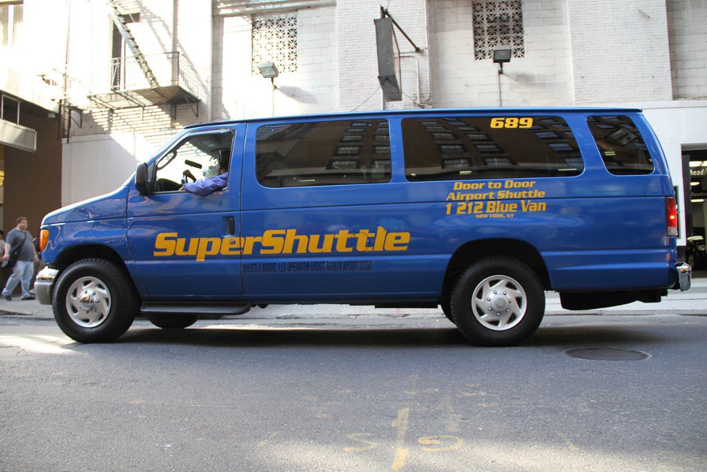 A SuperShuttle van is parked by the curb. 