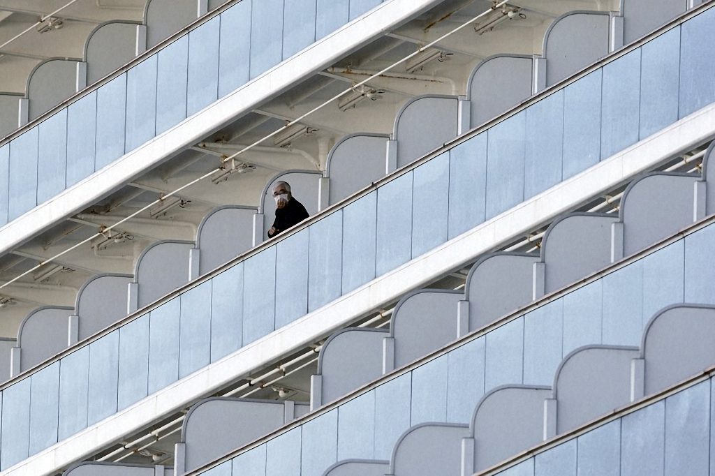 A passenger stands on the balcony of the Diamond Princess anchored at the Yokohama Port Thursday, Feb. 6., 2020, in Japan. The 3,700 people on board face a two-week quarantine in their cabins. Health workers said 10 more people from the Diamond Princess were confirmed sickened with the virus, in addition to 10 others who tested positive on Wednesday.
