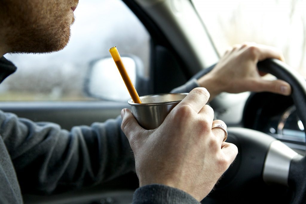 A person driving drinks through a reusable glass straw, a sustainable alternative to plastic.