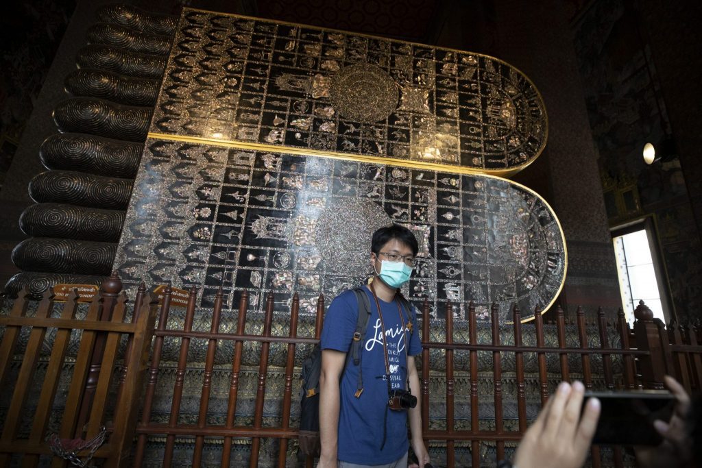 A masked tourist poses for a souvenir photo at Wat Pho, a popular Buddhist temple in Bangkok which has seen lesser crowds in recent weeks due to the virus scare.