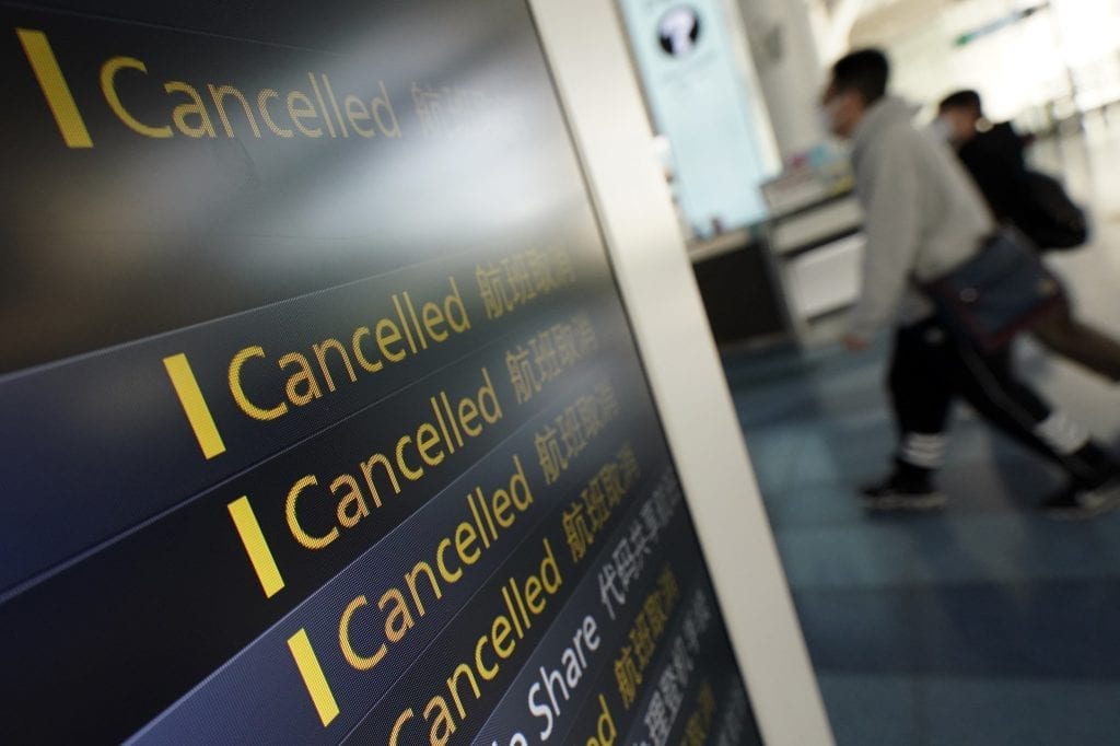 Travelers walk past canceled flights on a schedule board. 