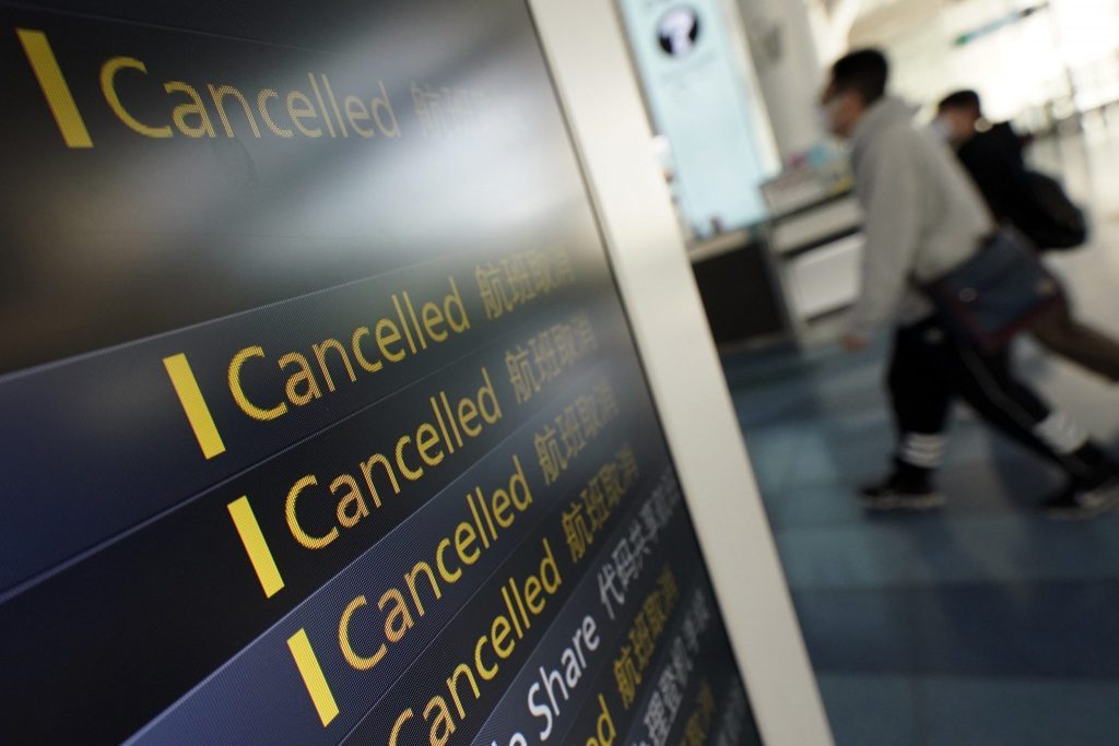 Travelers walk past canceled flights on a schedule board, some due to the coronavirus, at the Haneda International Airport in Tokyo. The flurry of travelers returning to their home countries in Asia has led to a spike in imported coronavirus cases, alongside a greater demand for hotels that double as self-quarantine venues. 