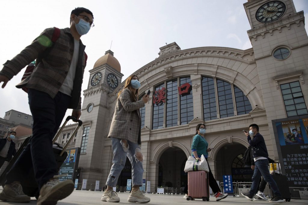 Travelers with their luggage walk past the Hankou railway station in Wuhan, China. Wuhan lifted its 11-week lockdown on April 8, allowing residents to travel in and out of the city. 