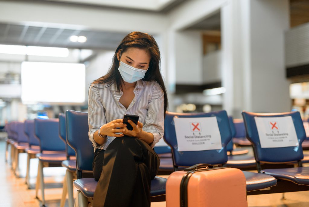 Young Asian traveler with mask socially distancing at an airport.