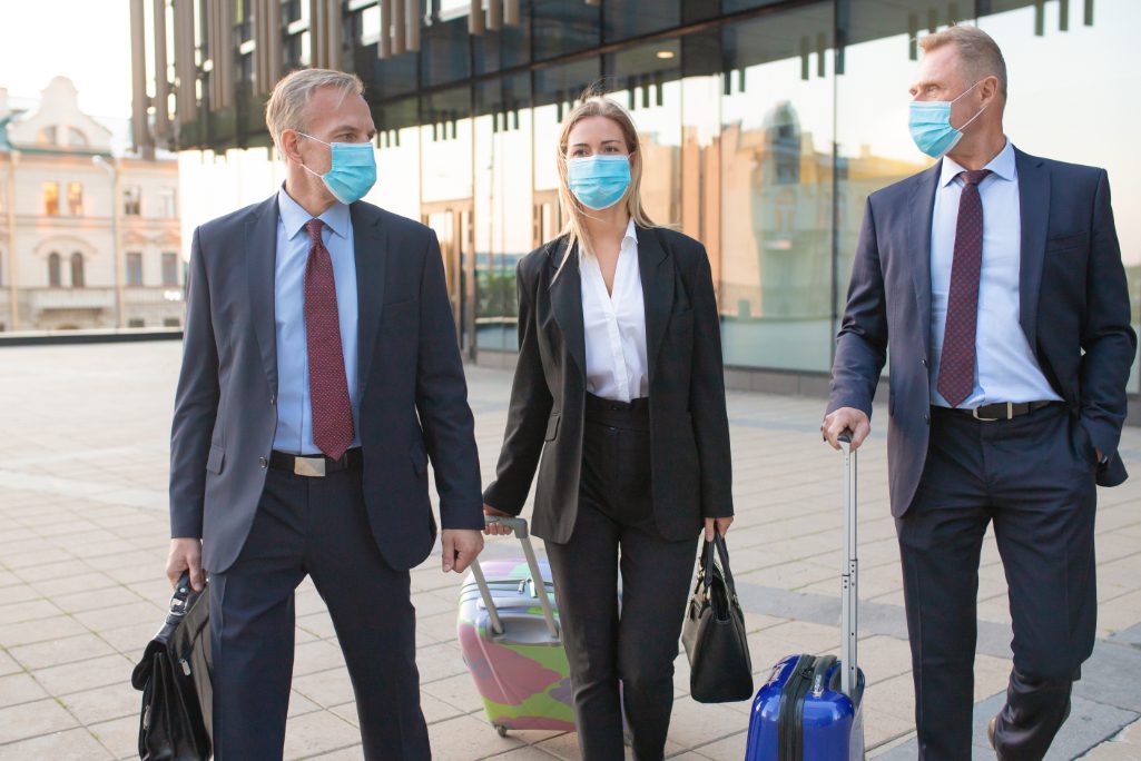 Business travelers wearing face masks walking outdoors with luggage during the pandemic. American Express Global Business Travel (GBT), a travel management company, recently signed $3 billion in new business, said CEO Paul Abbott.