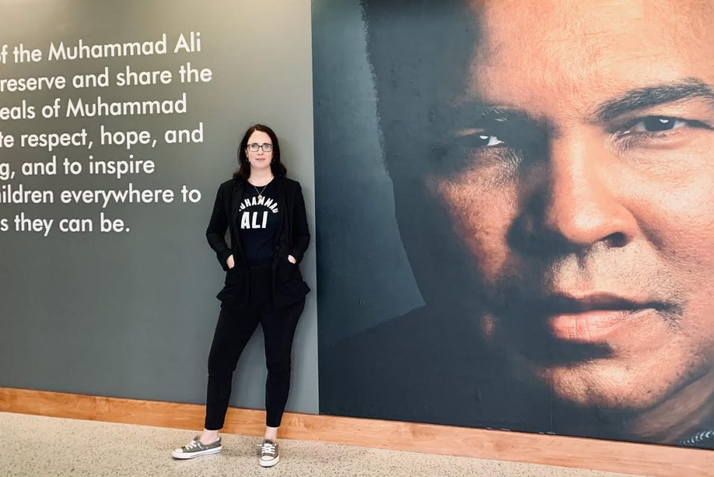 Educational programming director and tour guide Erin Herbert poses in front of a Muhammad Ali mural at the Ali Center in Louisville, Kentucky.