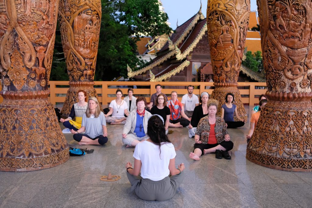 A group of travelers on a tour run by Pravassa meditating in Thailand.