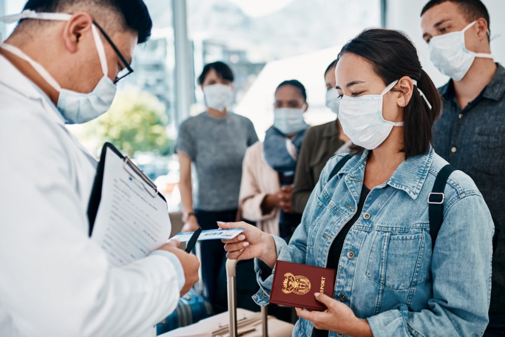 Shot of a woman wearing a mask and giving her passport to a doctor in an airport. Source: Getty Images.