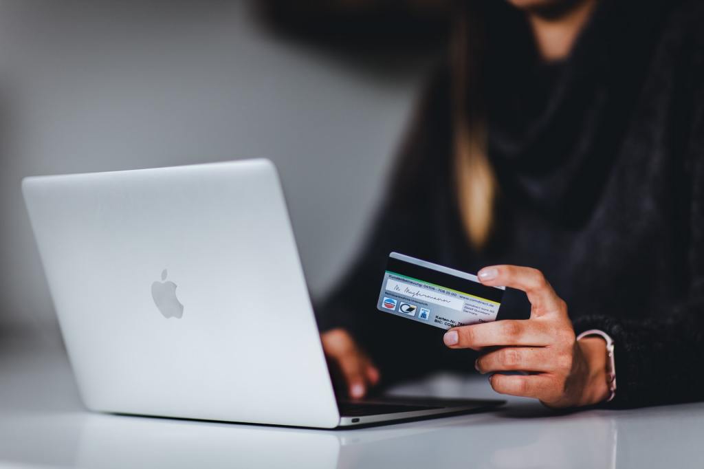 A woman holding a black credit card in front of a laptop