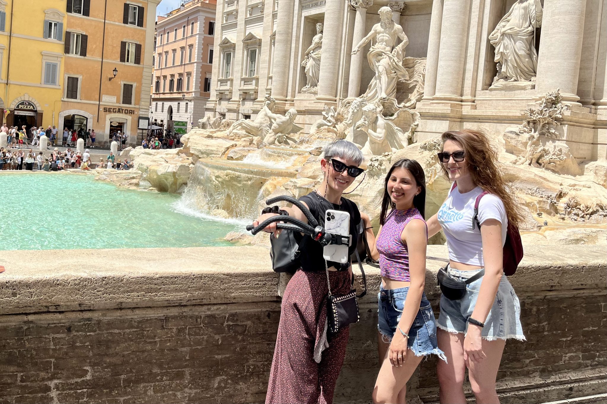 Three tourists with a selfie stick at Rome’s Trevi Fountain. 