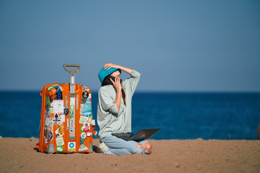A remote worker sits on the beach with a suitcase and works while on vacation. 