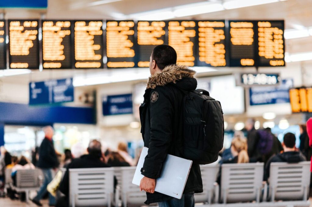 Man standing in front of airport flight board.