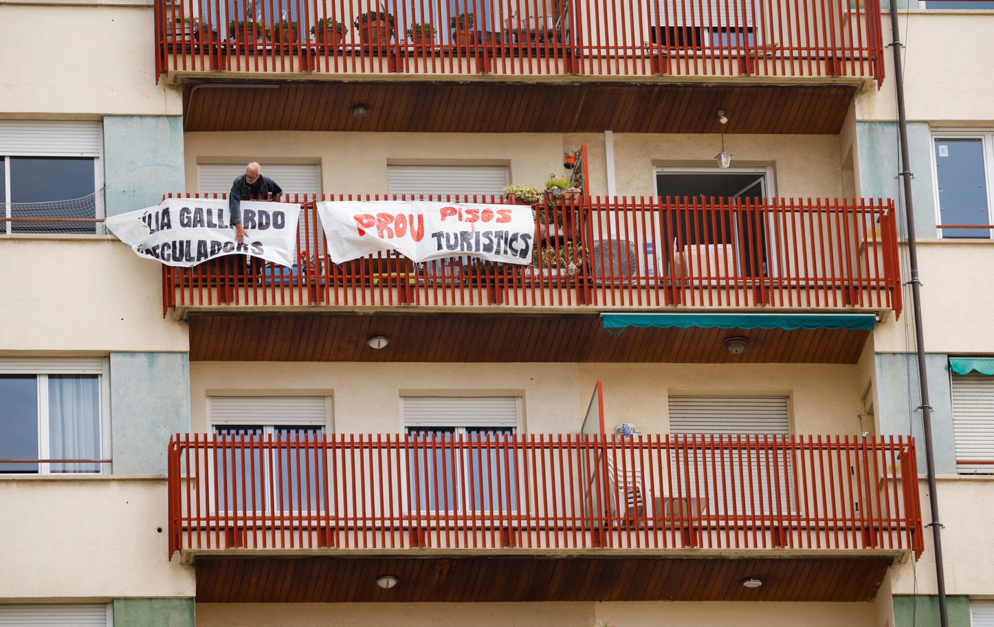 A man ties protest banners in the balcony of a building that was recently converted for tourist use at Sants neighborhood in Barcelona. Source: Reuters 