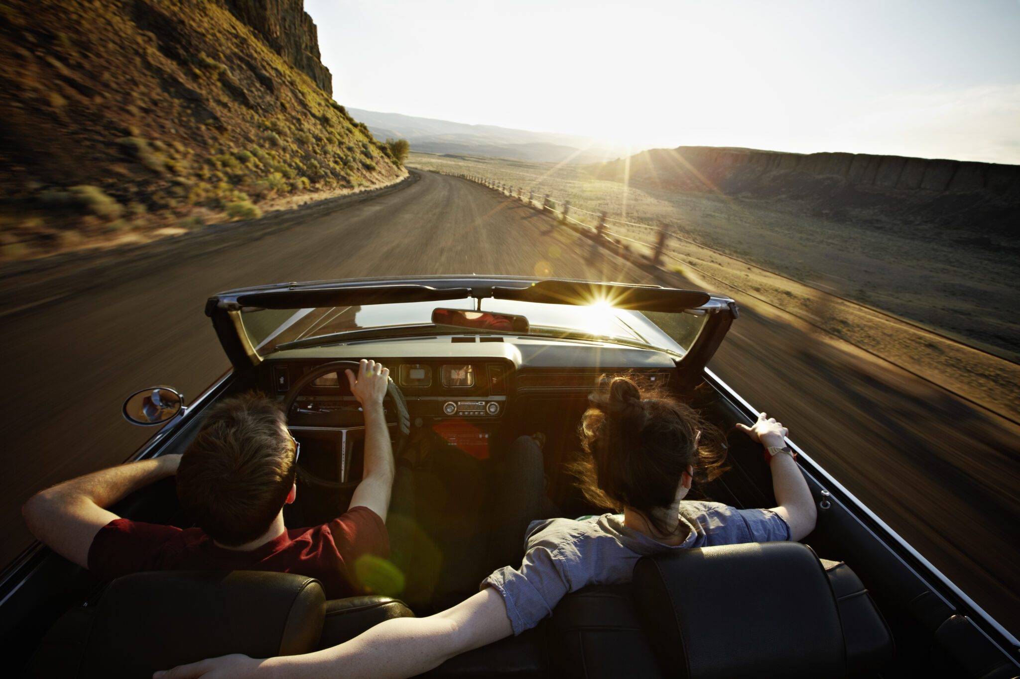Young couple driving convertible at sunset on desert road. Source: Getty Images/Thomas Barwick