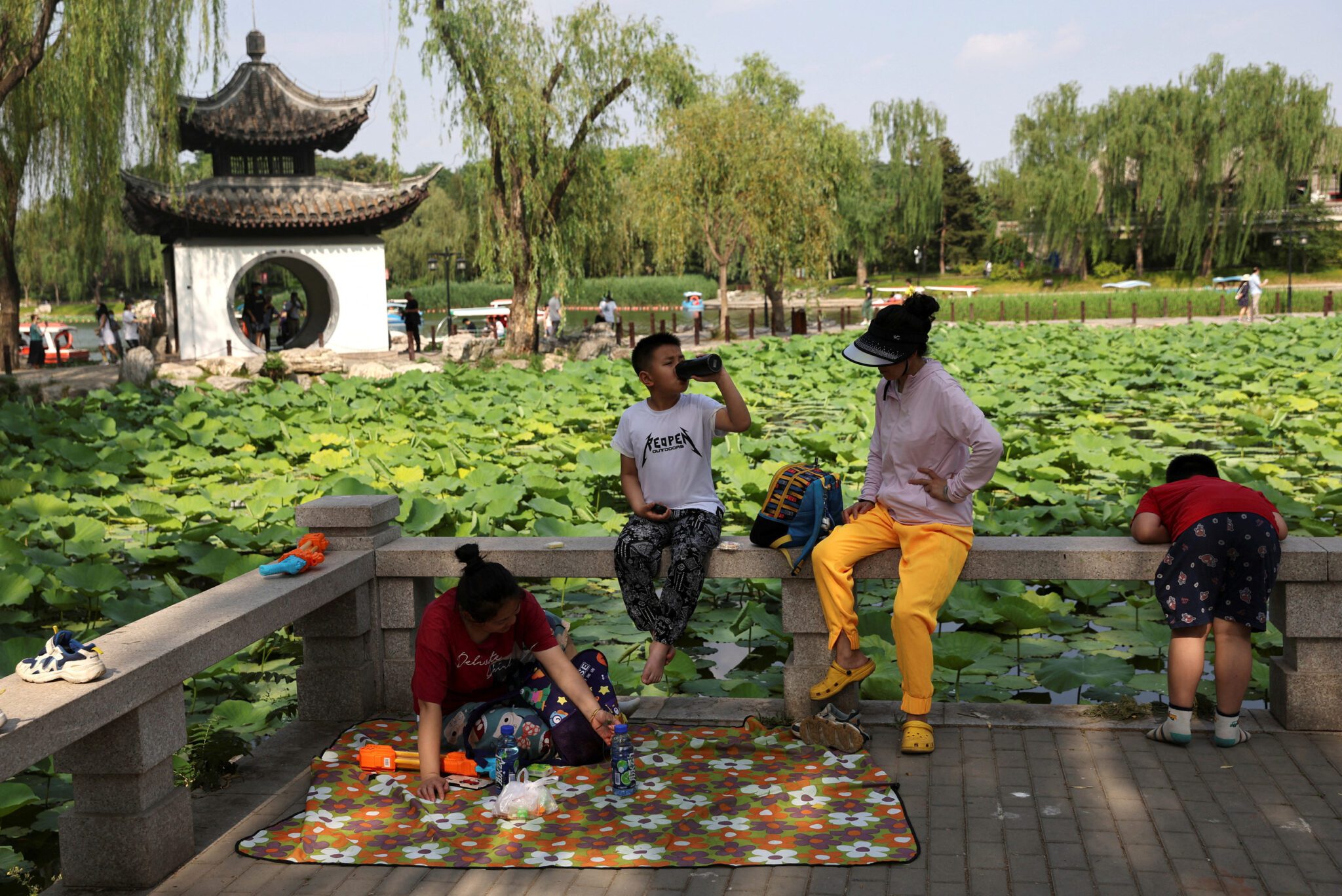 People and children enjoy themselves by the lakeside at a park during the Dragon Boat festival holiday in Beijing scaled. Source: Reuters