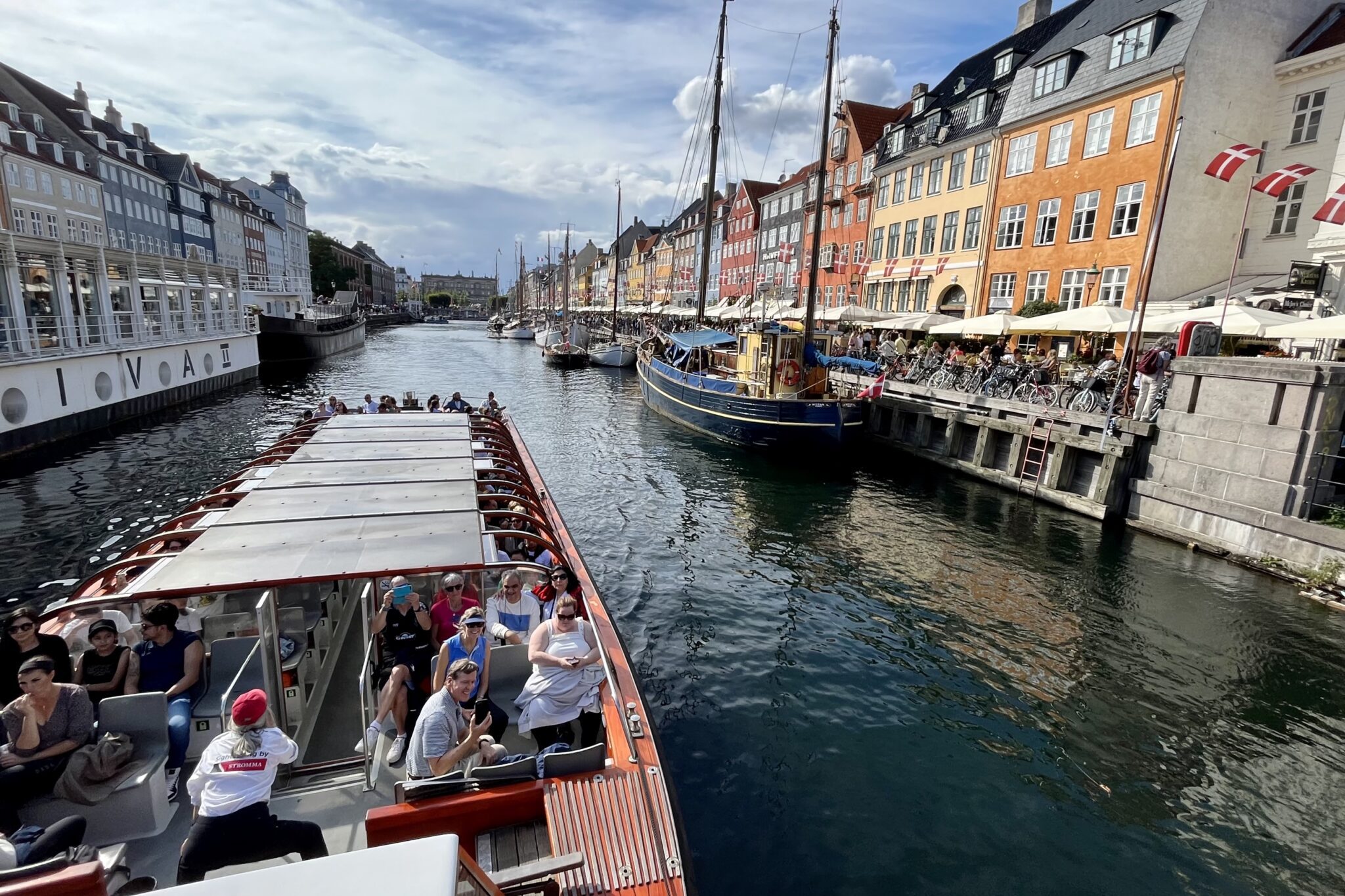 Tourists in a boat and alongside the shore of Copenhagen's Nyhavn canal. 