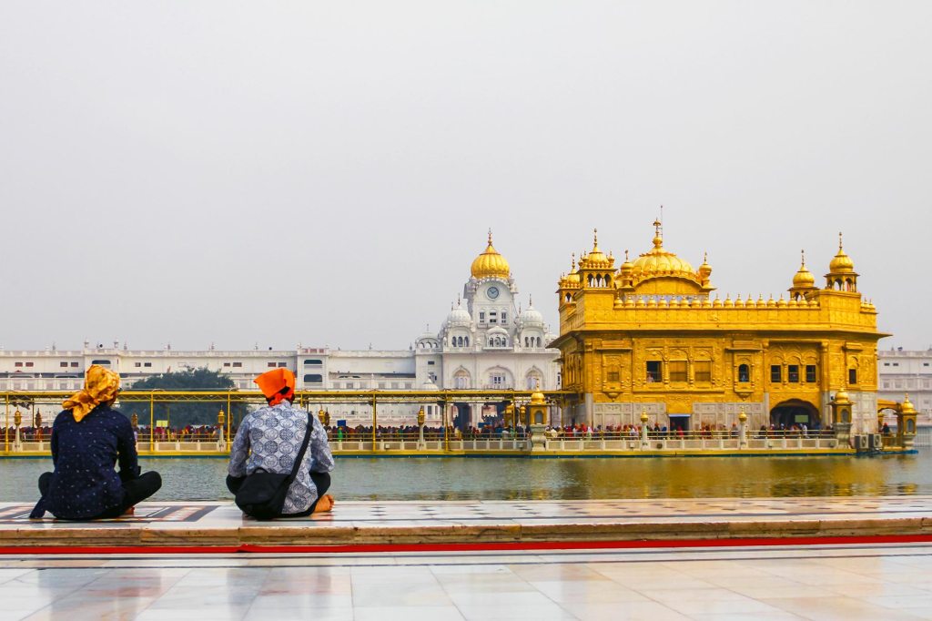 two figures seated with the the Golden Temple in Amritsar in the distance