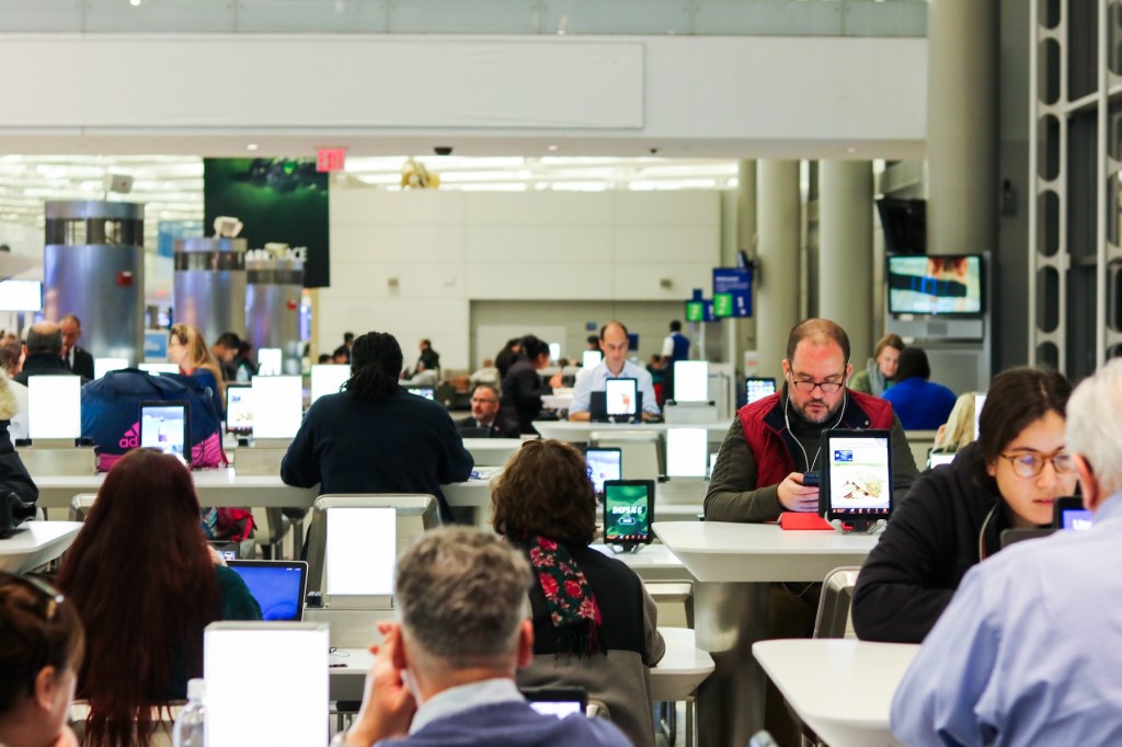 passengers wait at tables fitted with iPads at Newark's airport.