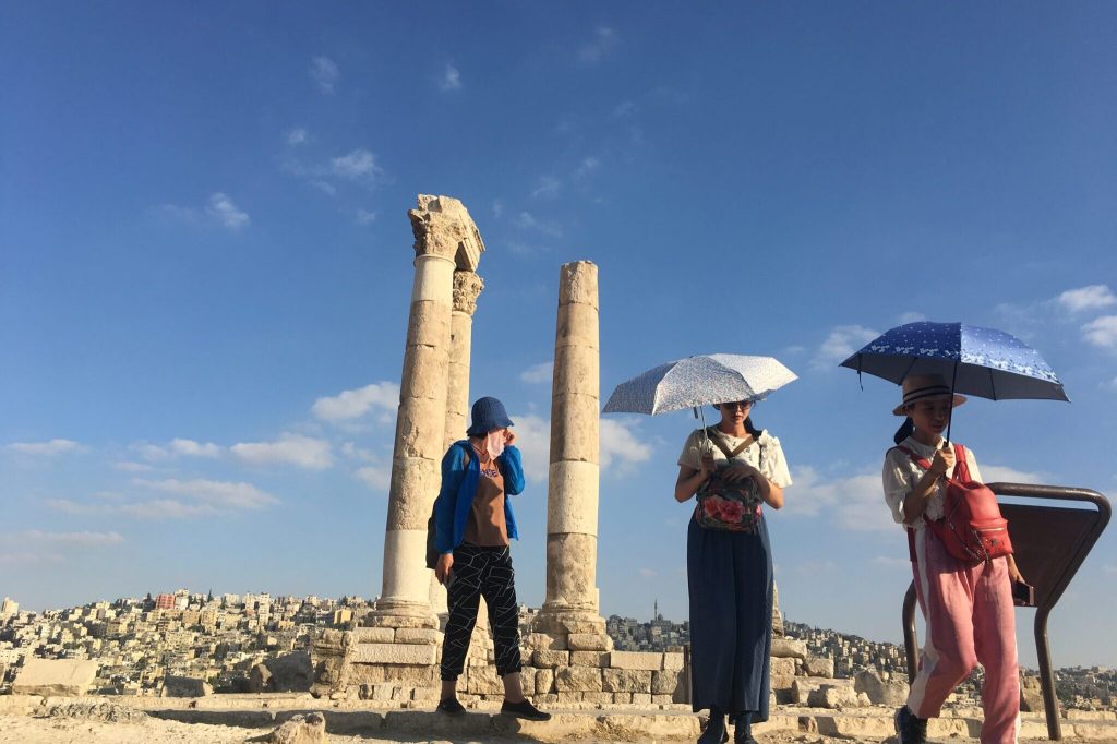 tourists with umbrellas protecting themselves from the Jordanian sun on a hill in Amman