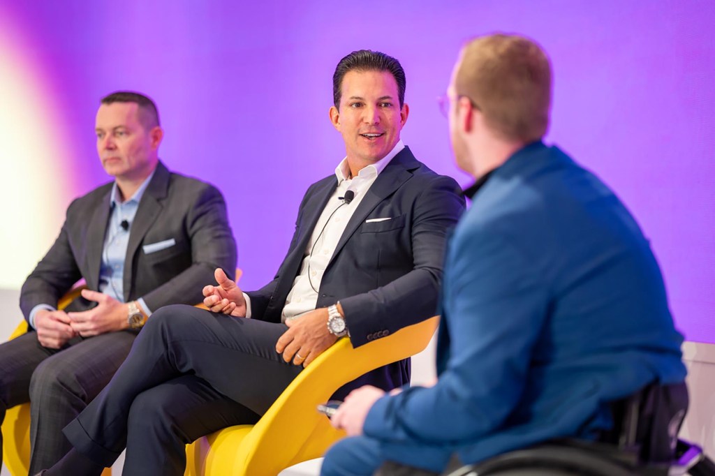 three men speaking onstage on a panel