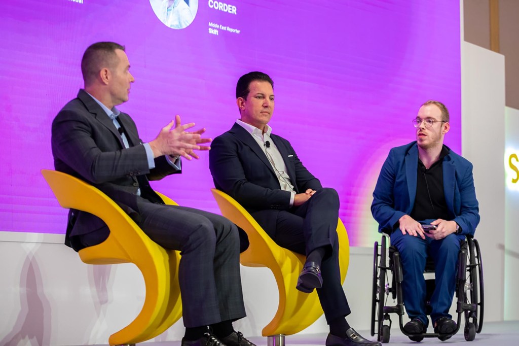 three men speaking onstage on a panel