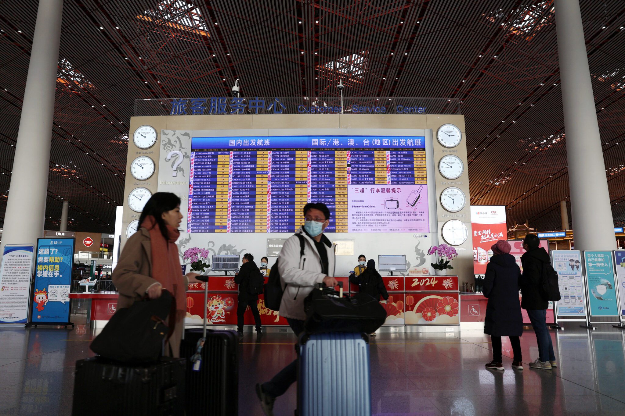 Travellers walk with their luggage past a display showing departure flights information at the Beijing Capital International Airport, during the Spring Festival travel rush ahead of the Chinese Lunar New Year, in Beijing, China February 2, 2024. REUTERS/Florence Lo/File photo