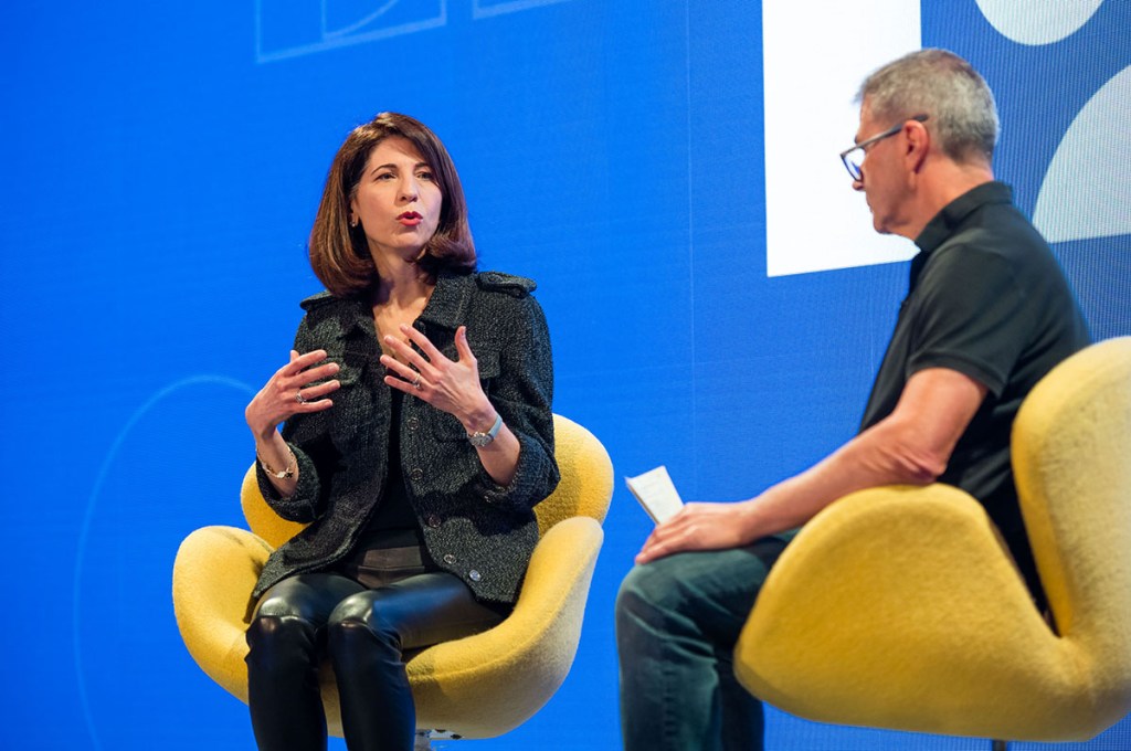 A woman talking to a man on stage at a conference.