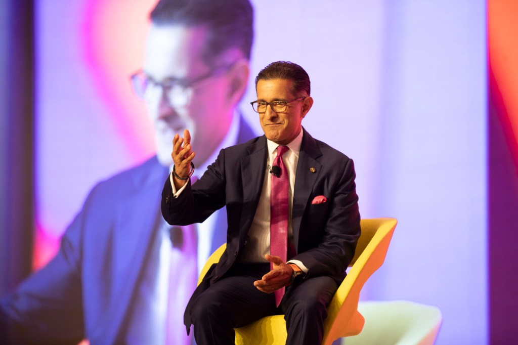 a man sitting in a yellow chair on stage with a video playing behind him