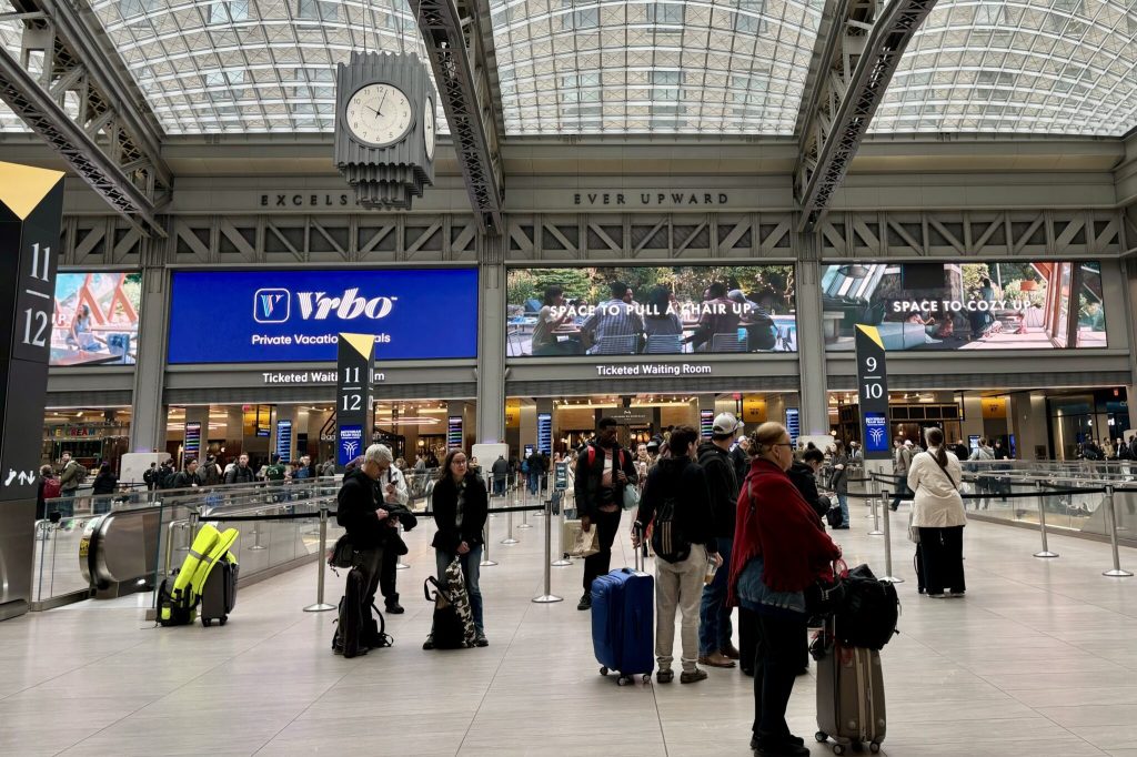 Crowded train station with large video advertisement boards in the background