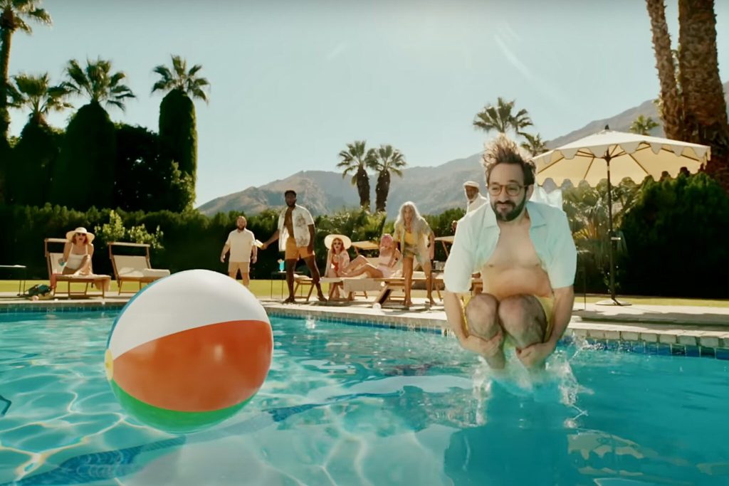 A man jumping into a pool next to a large Beachball