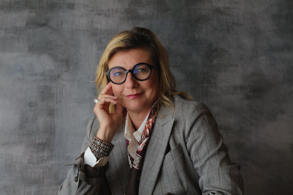 woman wearing statement eyeglasses against a grey background its barbara muckermann ceo kempinski hotels in a headshot