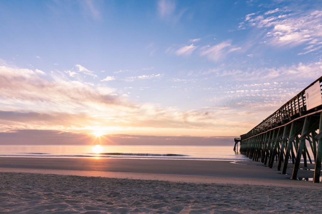 Pier to right on beach with a sunset