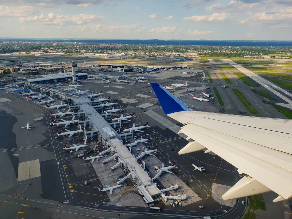 Wing of airplane in air overlooking airplanes on ground at airport