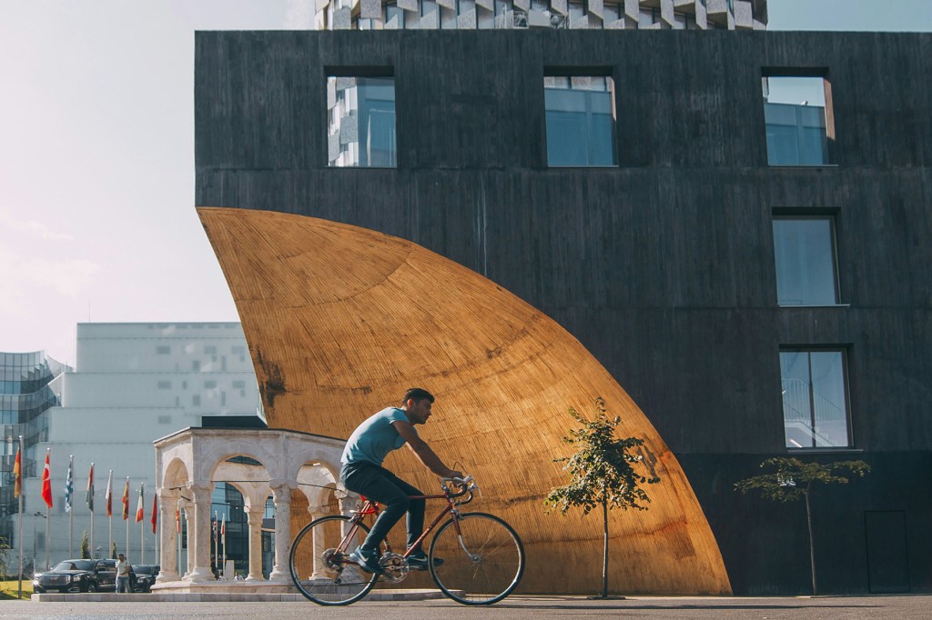 a cyclist on a street with a modern building behind him.