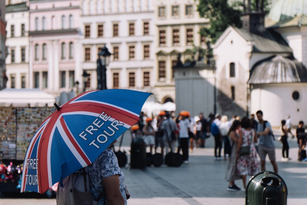 A person holding an umbrella that says "free tour" on a street.