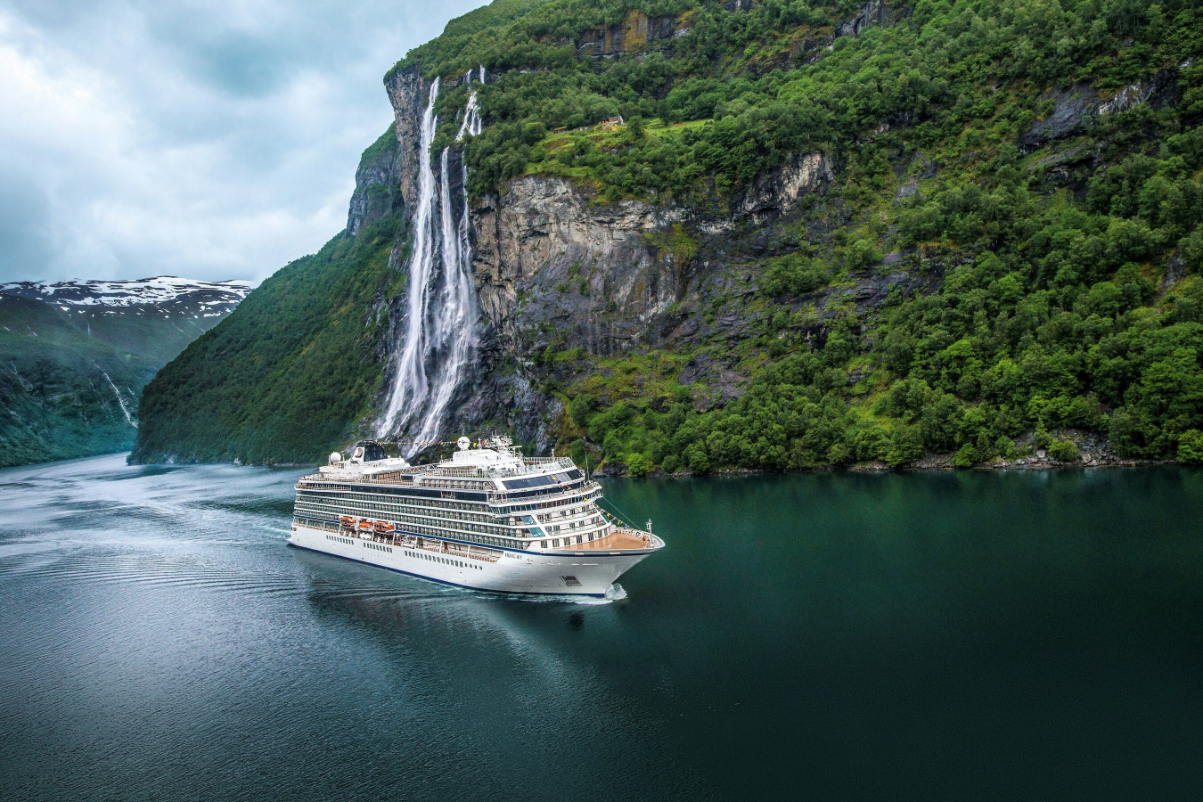 An aerial view of a cruise ship run by Viking Cruises, near Geiranger, Norway, and next to Seven Sisters Waterfall tumbling 1,000 feet into the fjord's water. Source: Viking Holdings