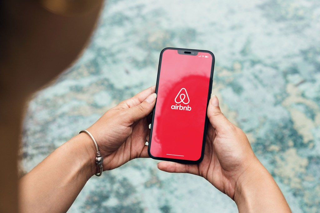 Woman in a park holding a smartphone with Airbnb app on the screen