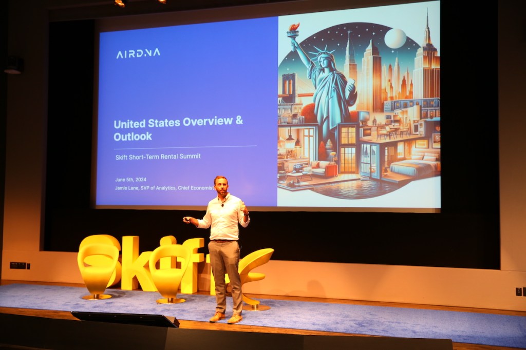 Man talking on stage with a presentation behind him that says, "United States Overview & Outlook"