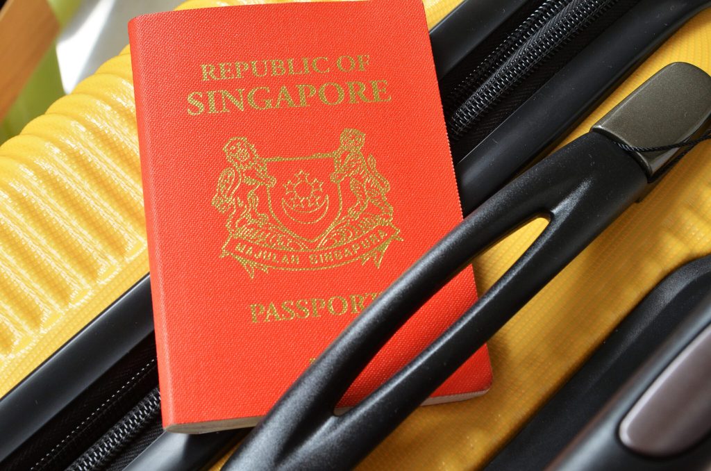 A Singaporean passport sitting atop a yellow suitcase.