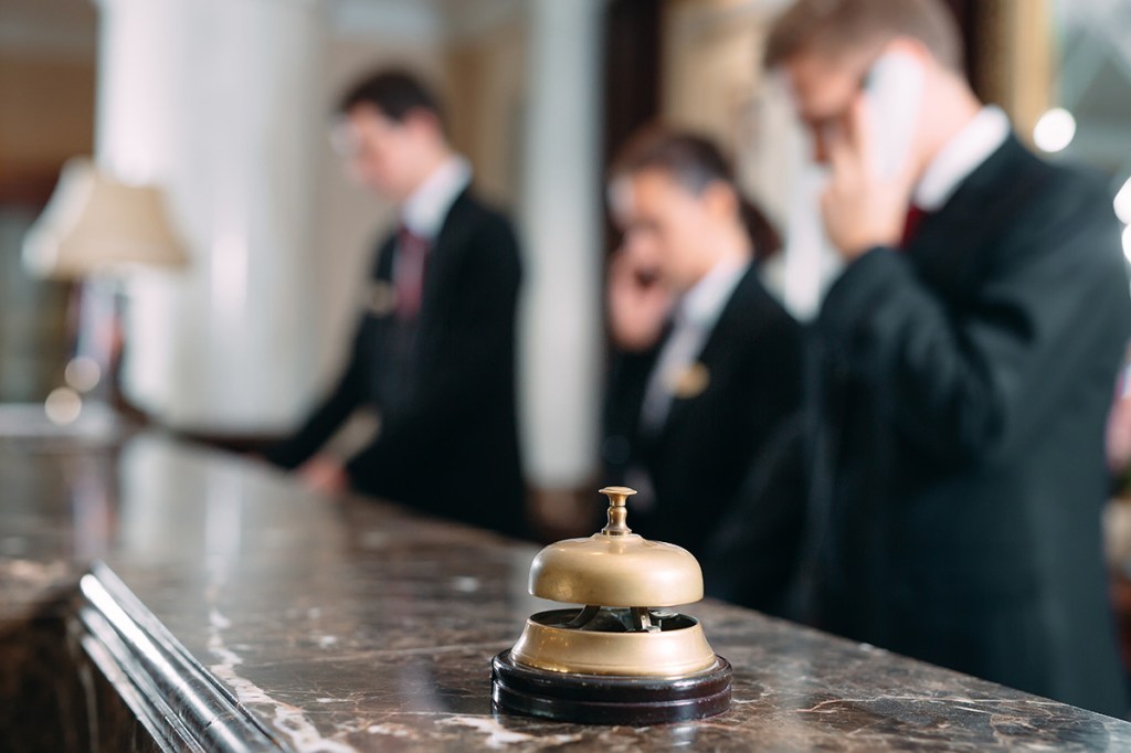 a bell sits on a hotel counter in front of three staff