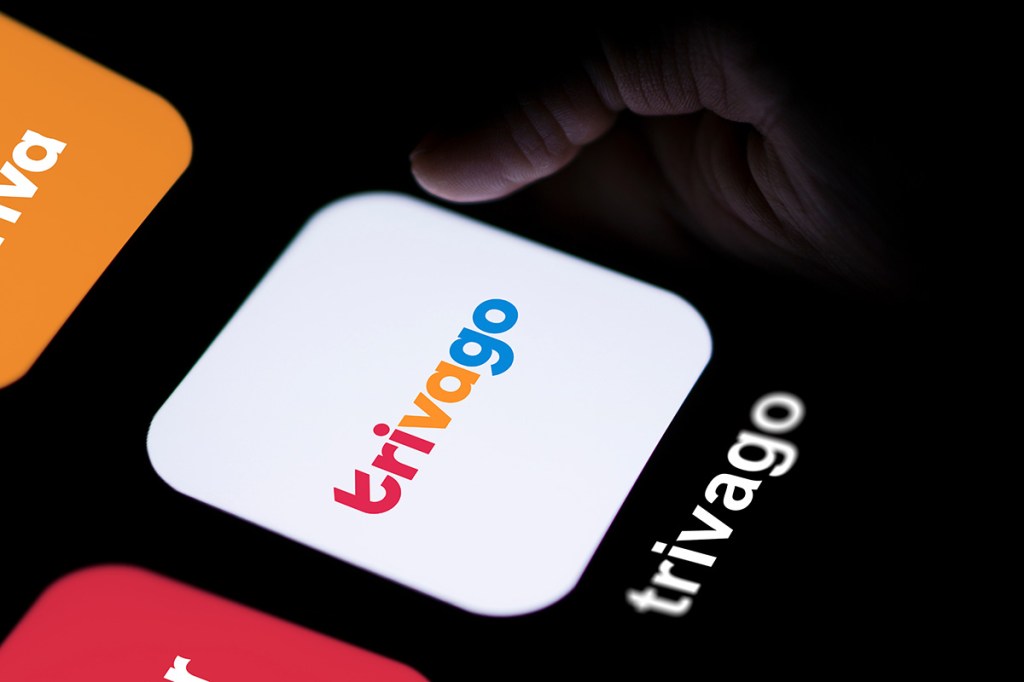 A finger touching a screen with the Trivago logo on the screen.